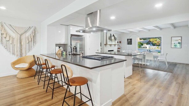 Een moderne keuken met een centraal eiland, barkrukken en een eethoek met uitzicht.