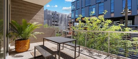 Un balcó amb taula i panqueta, plantes en testos i vista d'un paisatge urbà amb edificis moderns.