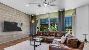 A modern living room with a leather sofa, a glass coffee table, and a flat-screen TV mounted on a brick wall. - Exquisite apartment with 2 balconies - Pool!! (Tempe)