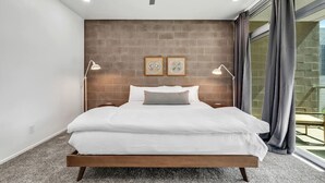 Une chambre moderne avec un mur d’accent en briques, deux lampes de chevet et un grand lit.