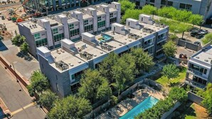 Un bâtiment moderne doté de plusieurs terrasses sur le toit, d’une piscine et d’un espace verdoyant environnant.