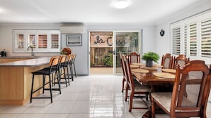 Une cuisine moderne avec un coin repas, comprenant un grand îlot central, des chaises en bois et une vue sur un jardin extérieur, accessible par une porte vitrée.