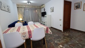 A dining area with a table set for two, a sofa, and a TV on the wall. - BENIBEACH (1 BEDROOM) (Benidorm)