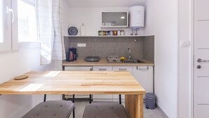 Una pequeña kitchenette con una mesa de madera, dos taburetes acolchados, un microondas, un fregadero y un cubo de basura.