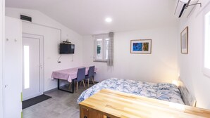 Un dormitorio con una cama de madera, un escritorio y una silla. Hay un televisor montado en la pared y una ventana con cortinas.