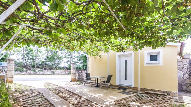 Un patio techado con una mesa, sillas, una puerta y un muro de piedra.