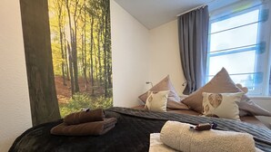 A bedroom with a bed, pillows, a blanket, and a forest-themed wall mural. - Waldläufer Brilon (Brilon)
