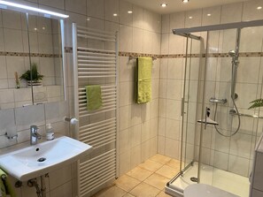 A modern bathroom with a glass shower enclosure, a white sink, and a towel rack.