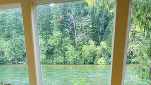 A dining table set for two with a view of a river and forest through large windows.