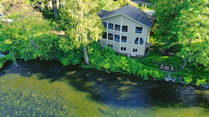 Et toetagers hus med balkon, omgivet af frodig vegetation og en flod.