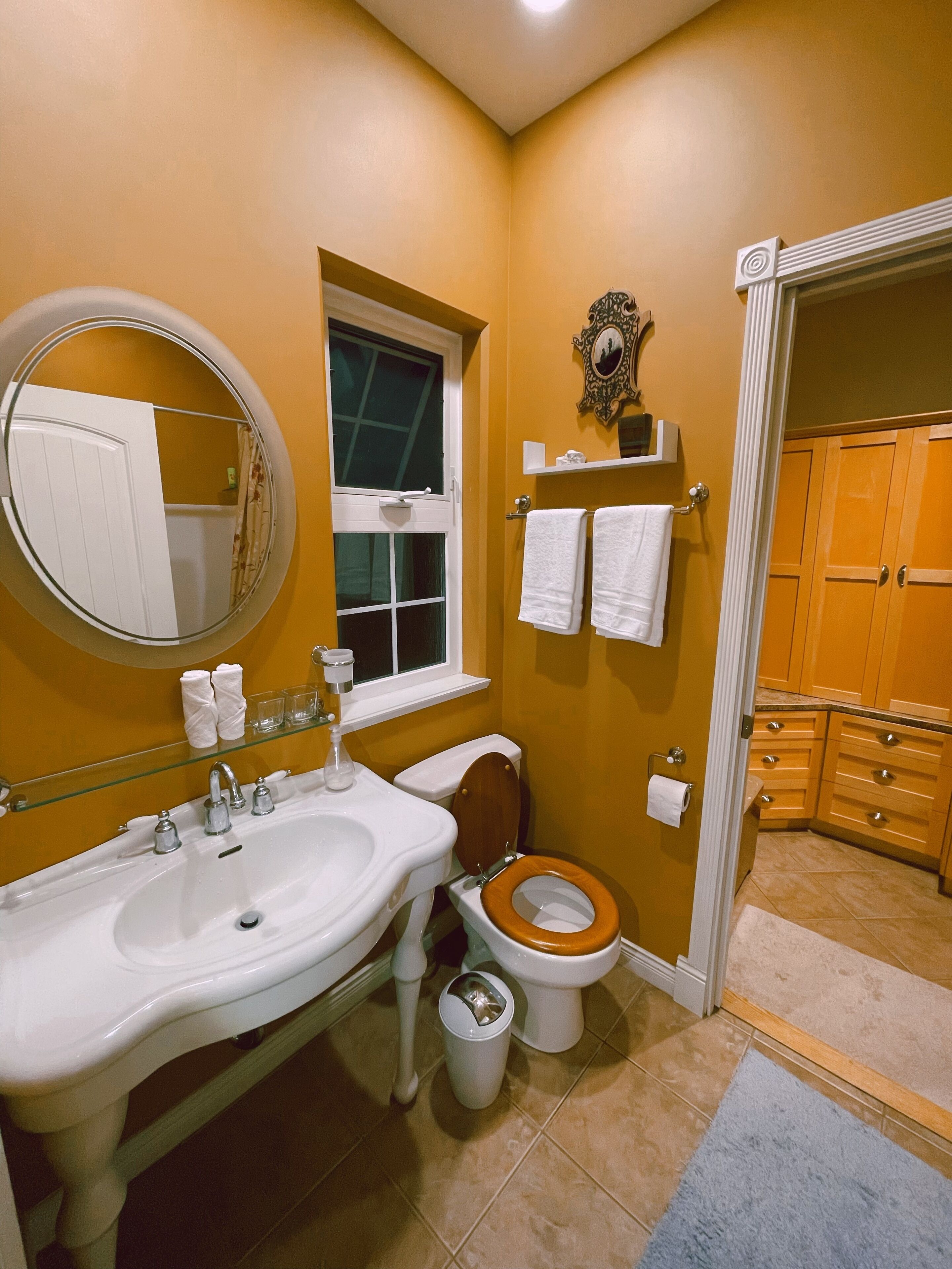 A bathroom with a white sink, a toilet, and a mirror. There is a window above the sink and a towel rack above the toilet.