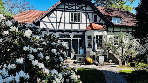 A traditional half-timbered house with a red-tiled roof, a paved driveway, and a garden with white flowers. - Zirkuswagen am Landhaus Labes (Stechlin)