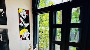 A room with a wooden chair, a fur-covered sofa, and a glass table with a candle. There are paintings on the wall and a view of greenery outside. - Zirkuswagen am Landhaus Labes (Stechlin)