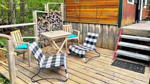 A wooden deck with outdoor furniture, a stack of firewood, and a cabin with a wooden exterior. - Zirkuswagen am Landhaus Labes (Stechlin)