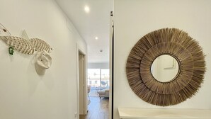 Um corredor com uma escultura de peixe na parede, um espelho redondo e um armário branco com gavetas.
