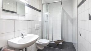 A modern bathroom with a white sink, toilet, and glass shower enclosure. - Landgasthof Krone (Offingen)