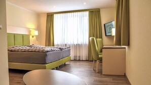 A hotel room with a bed, a desk, a chair, a small table, and a mirror. - Landgasthof Krone (Offingen)
