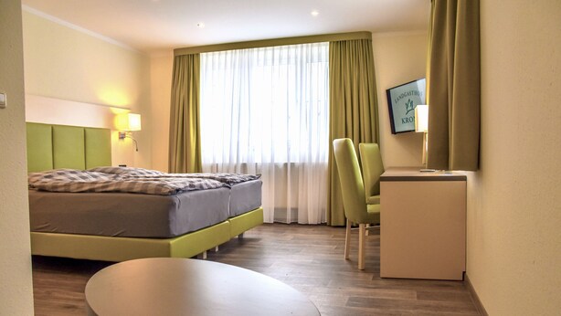 A hotel room with a bed, a desk, a chair, a small table, and a mirror. - Landgasthof Krone (Offingen)