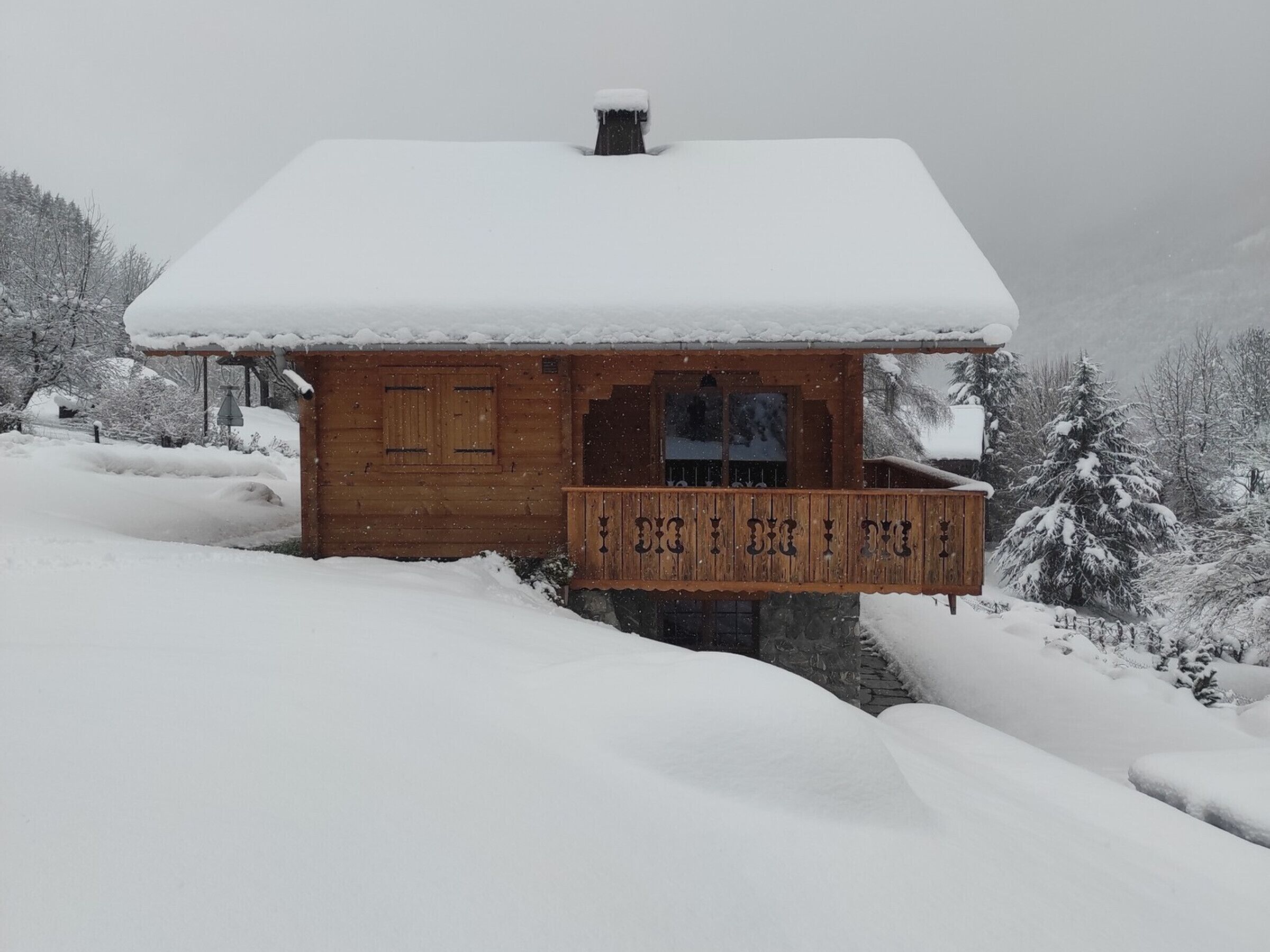 Una cabaña de madera con techo nevado y un balcón.