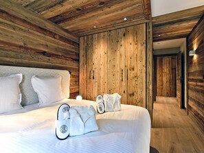A modern bedroom with a wooden ceiling and walls, a large bed with white bedding, and slippers on the bed. - Ski-in ski-out apartment with concierge in Méribel (Méribel)