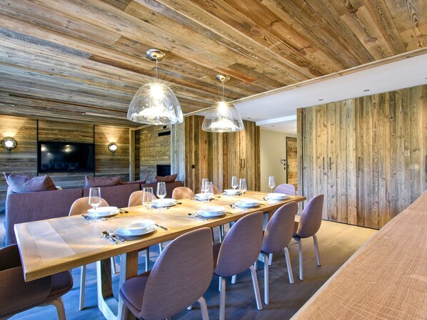 A modern dining area with a long wooden table set for six, surrounded by cushioned chairs. - Ski-in ski-out apartment with concierge in Méribel (Méribel)