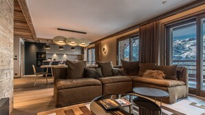 A modern living room with a sectional sofa, a coffee table, and a dining area with a kitchen in the background. - Superb ski-in/ski-out apartment with 5* concierge, Méribel (Méribel)