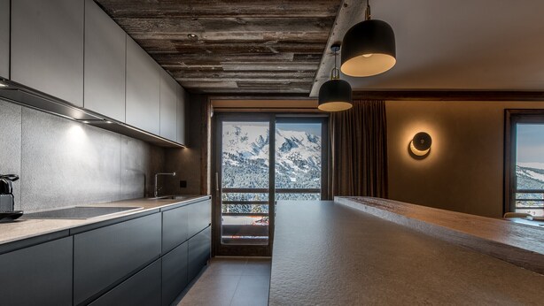 A modern kitchen with dark cabinetry, a wooden ceiling, and a large window offering a mountain view. - Superb ski-in/ski-out apartment with 5* concierge, Méribel (Méribel)