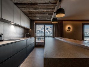 Eine moderne Küche mit dunklen Schränken, Holzbalkendecke und einem großen Fenster mit Blick auf die Berge.