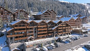 A multi-story wooden lodge with balconies, a parking area, and a view of snow-covered mountains. - Superb ski-in/ski-out apartment with 5* concierge, Méribel (Méribel)