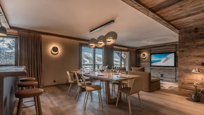 A modern living room with a wooden ceiling, a large TV mounted on the wall, and a dining area with a wooden table and chairs. - Superb ski-in/ski-out apartment with 5* concierge, Méribel (Méribel)