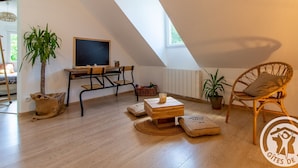 A cozy loft-style room with a sloped ceiling, a wooden desk with a chalkboard, two chairs, a small table, and a large window. - Cozy Gîte with Shared Heated Pool near Angers (Tiercé)