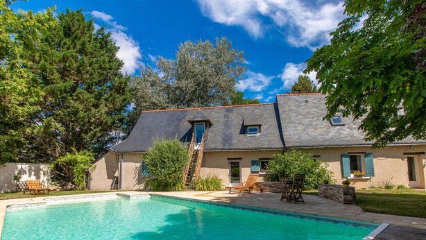 A swimming pool with a wooden deck, a house with a sloped roof, and a clear blue sky. - Cozy Gîte with Shared Heated Pool near Angers (Tiercé)