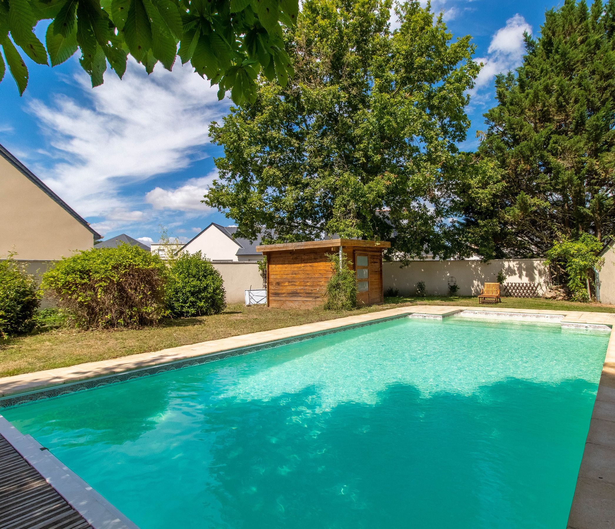 A swimming pool with a wooden deck, surrounded by trees and a small wooden structure.