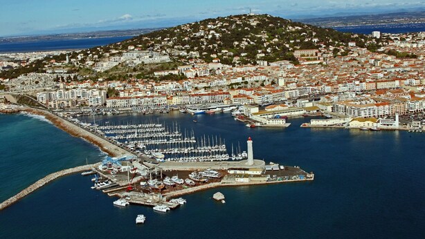 An aerial view of a coastal town with a marina, buildings, and a hill in the background. - 2-room mezzanine, private parking, pets allowed (Sète)