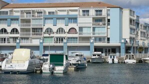 A marina with several boats docked in front of a multi-story building with balconies. - 2-room mezzanine, private parking, pets allowed (Sète)