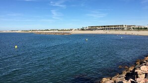 A coastal view with a sandy beach, a rocky shoreline, and a building with multiple balconies overlooking the sea. - 2-room mezzanine, private parking, pets allowed (Sète)