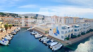 A marina with boats docked along a waterfront, surrounded by buildings with arched windows and a sailboat mural. - 2-room mezzanine, private parking, pets allowed (Sète)