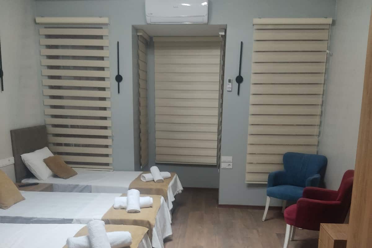 A hotel room with multiple beds, a blue chair, a red chair, and a wooden cabinet.