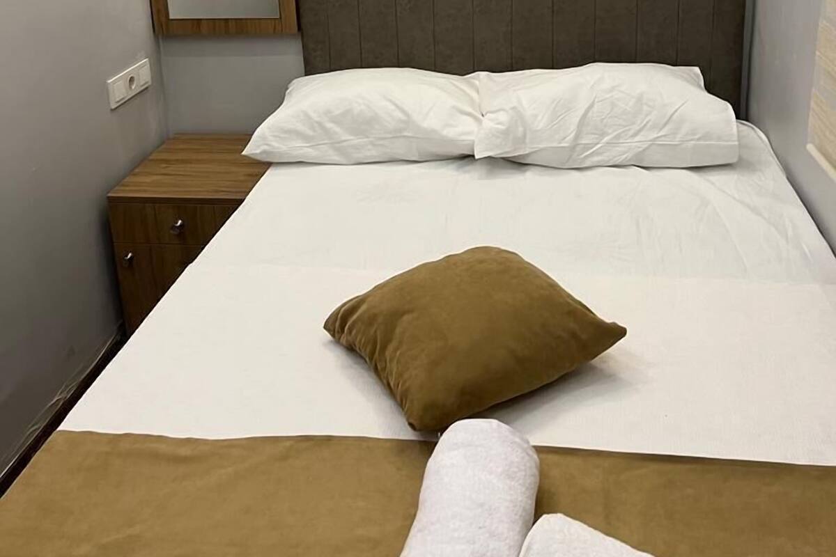 A neatly made bed with white and brown bedding, a brown pillow, and a brown towel. A mirror is mounted on the wall to the left.