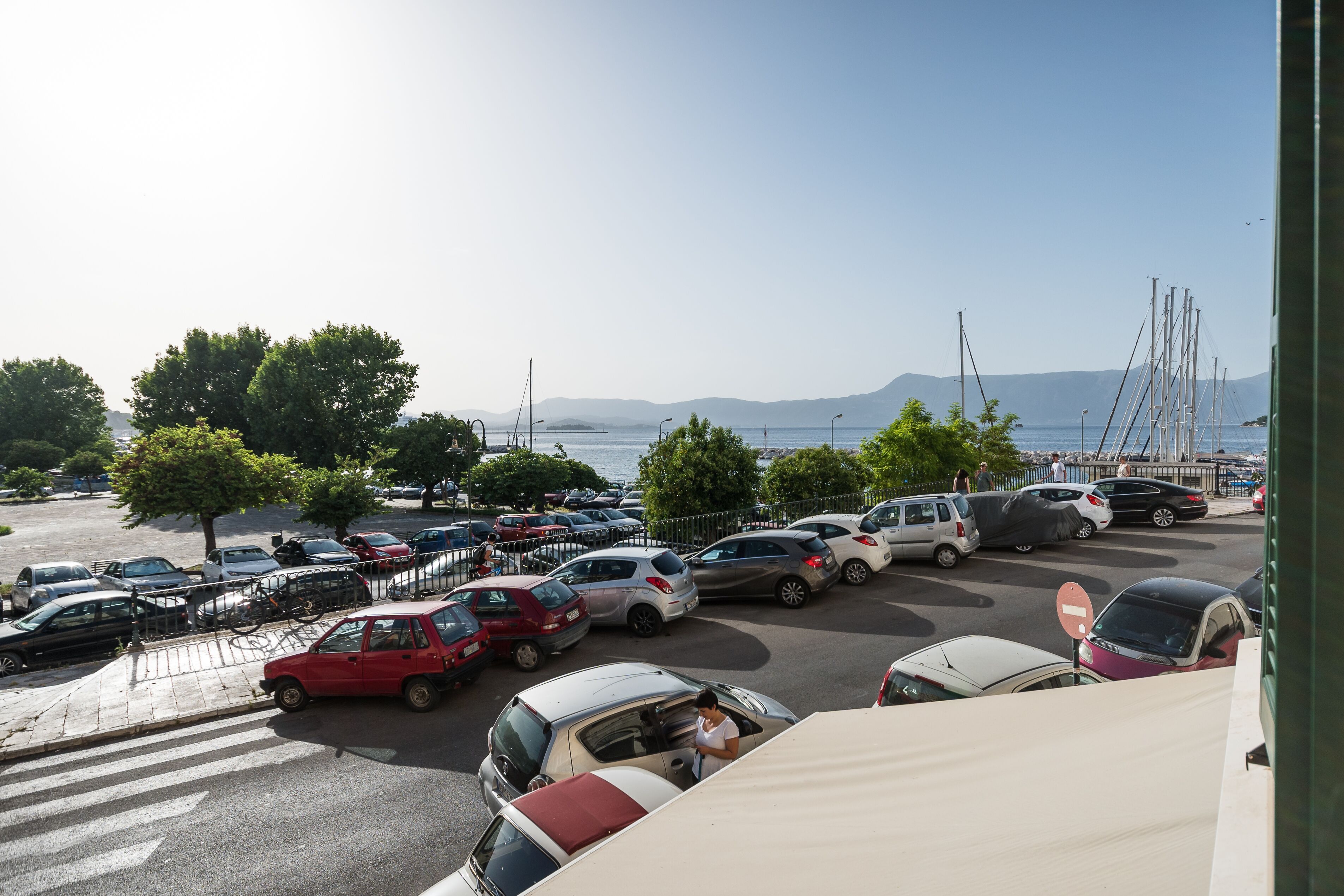 Un parking rempli de voitures, avec une vue sur la mer et les montagnes en arrière-plan.