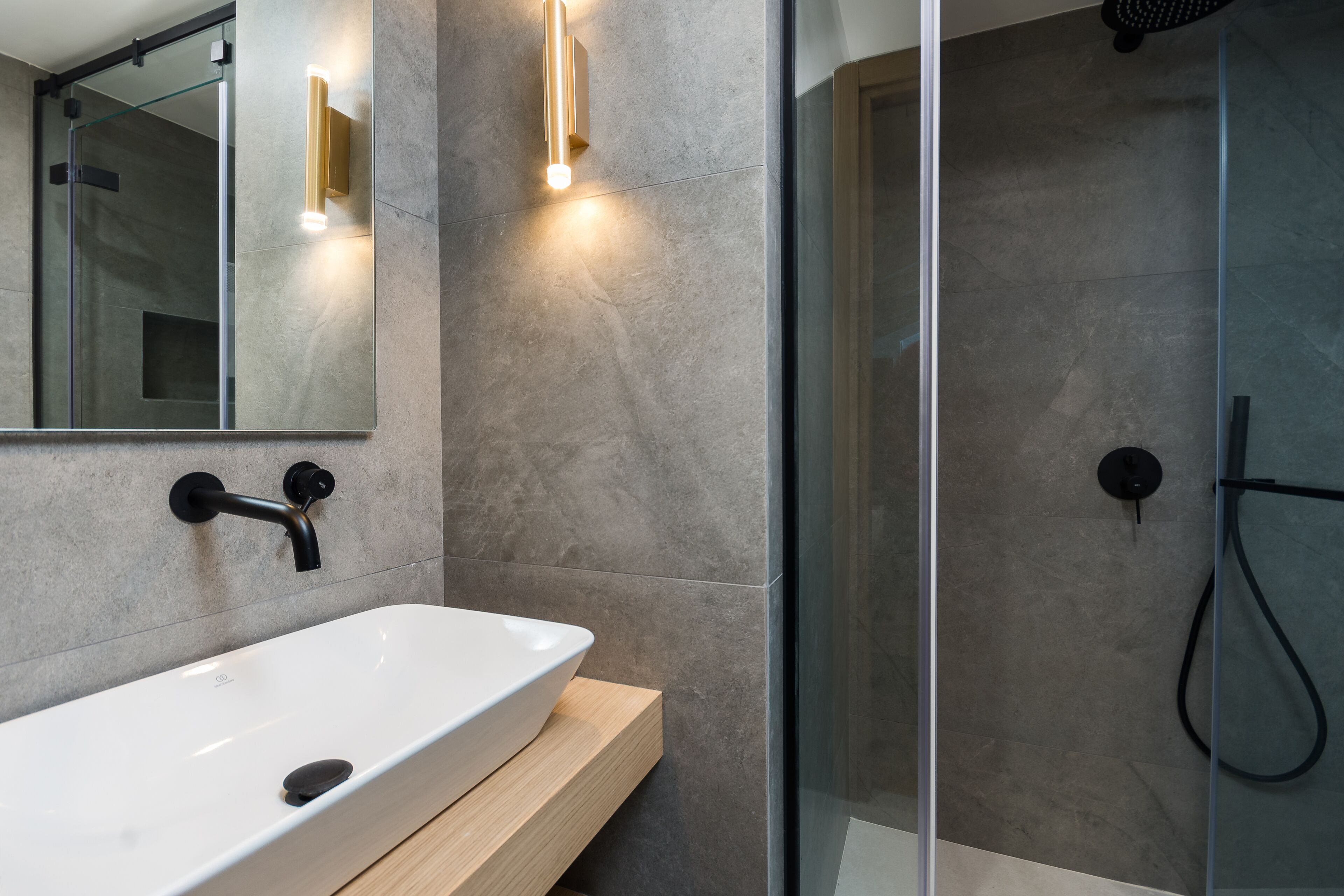 Un baño moderno con un lavabo blanco, cabina de ducha con paredes de cristal y mueble de tocador de madera.