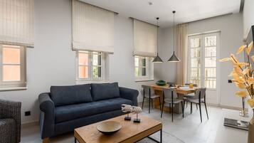 A modern living room with a dark blue sofa, a wooden coffee table, and a dining area with a table and chairs.