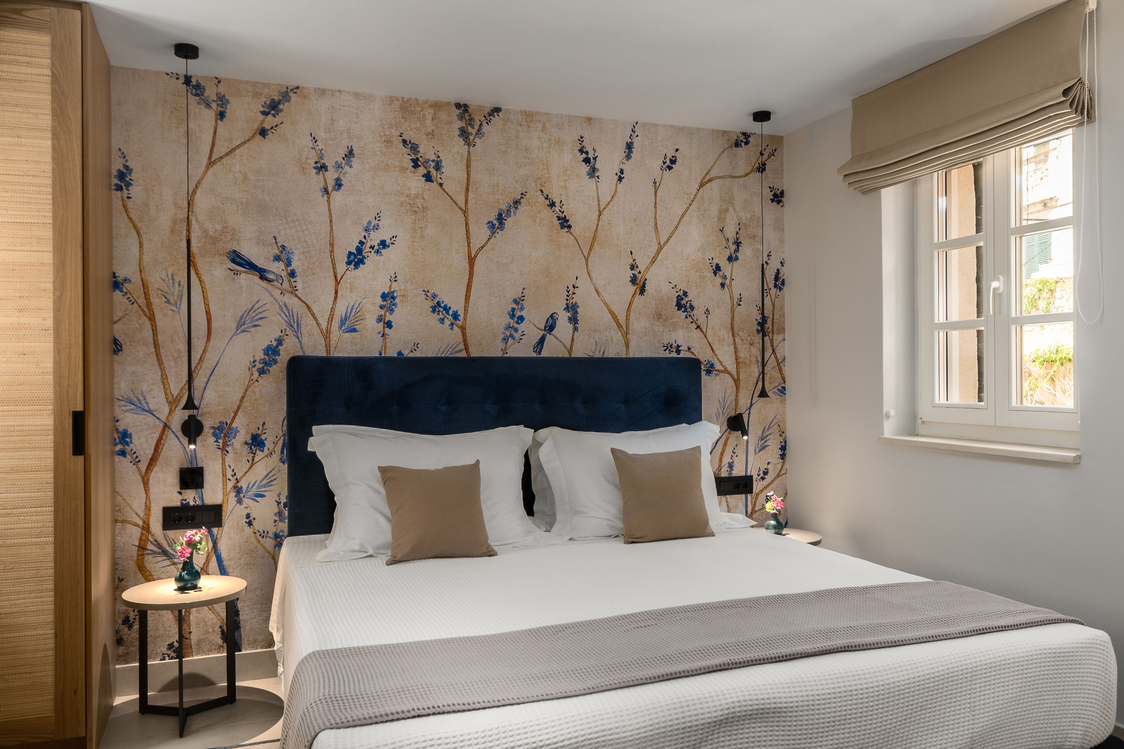 A bedroom with a large bed, a headboard, a round side table, and a wall with a floral pattern.