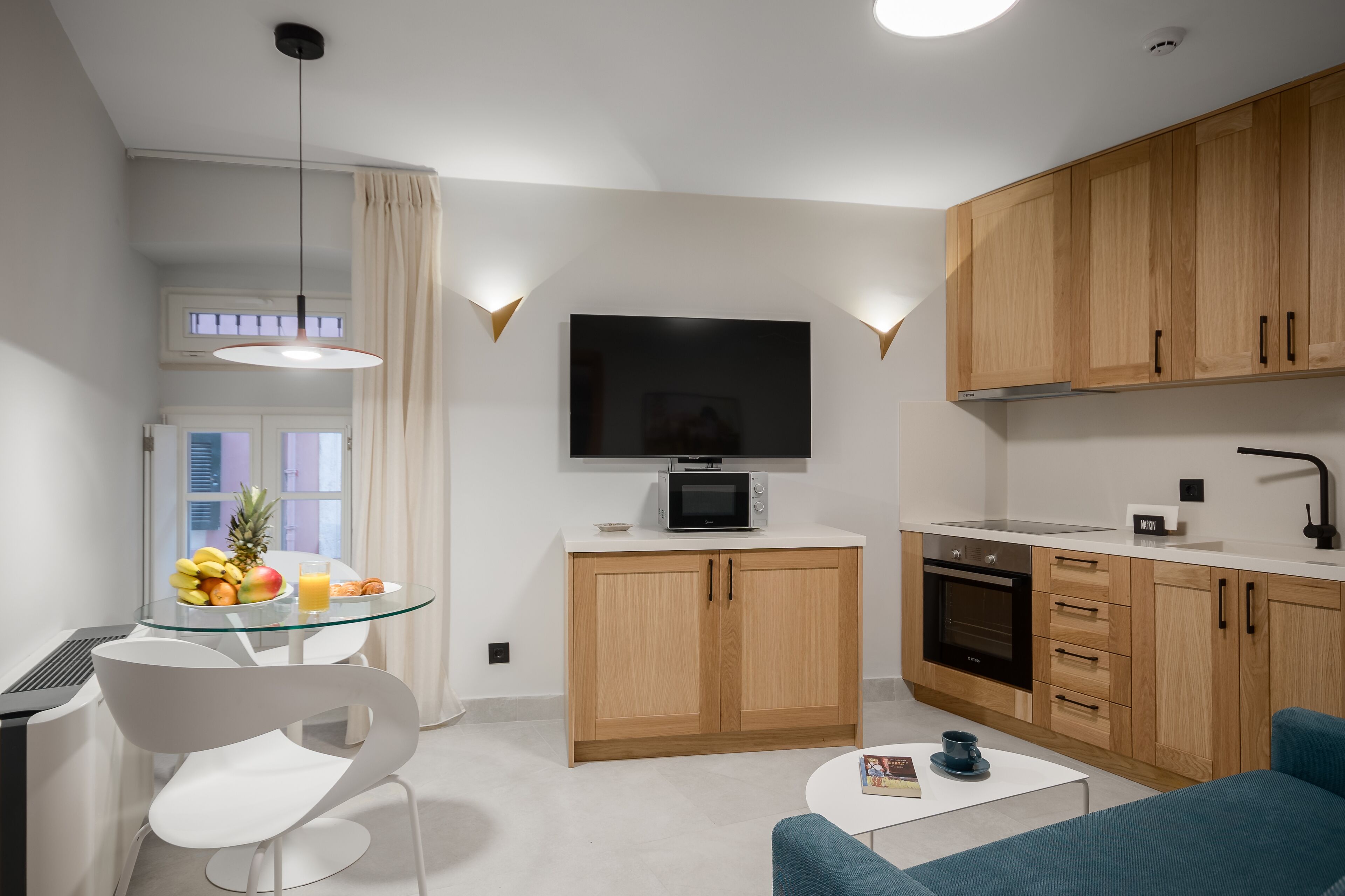 A modern kitchen with wooden cabinets, a microwave, and a dining area with a glass table and white chairs.