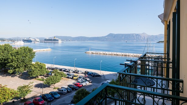 Uitzicht op de kust vanaf een balkon, met zicht op een jachthaven, geparkeerde auto's en een cruiseschip in de verte.