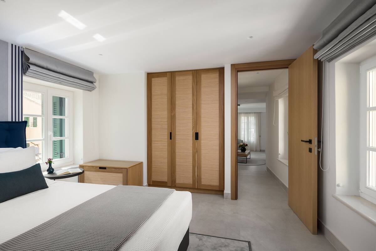 A bedroom with a bed, bedside table, wooden wardrobe, and a view into another room.