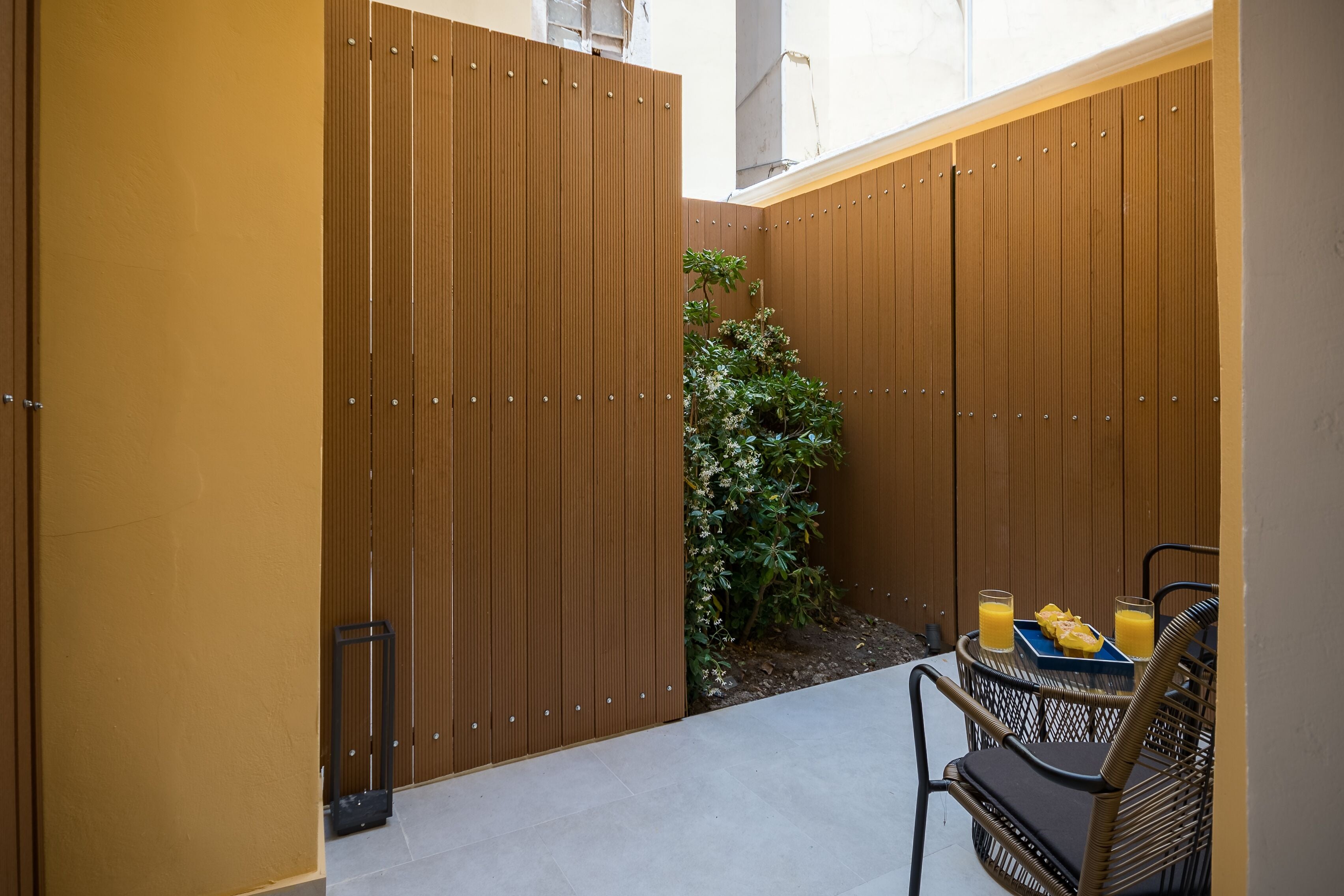 A small outdoor seating area with a table and chairs, a wooden fence, and a potted plant.