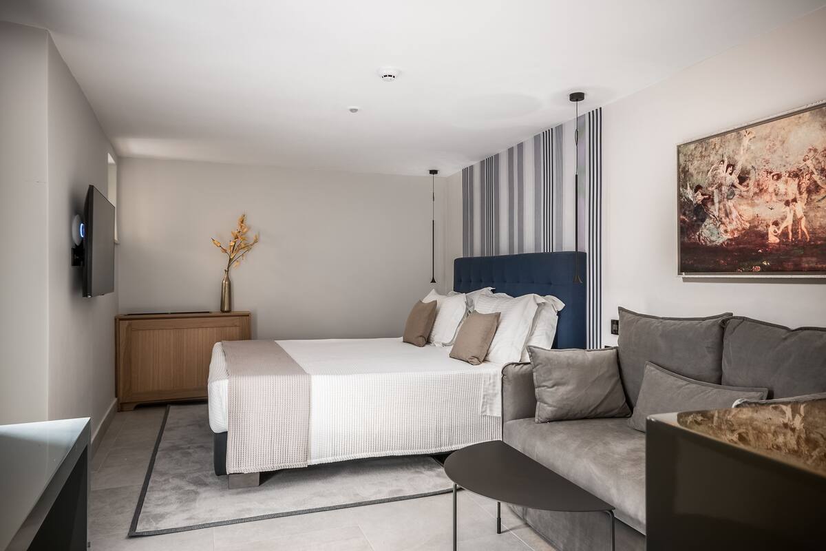 A modern bedroom with a bed, a sofa, a TV, and a painting.
