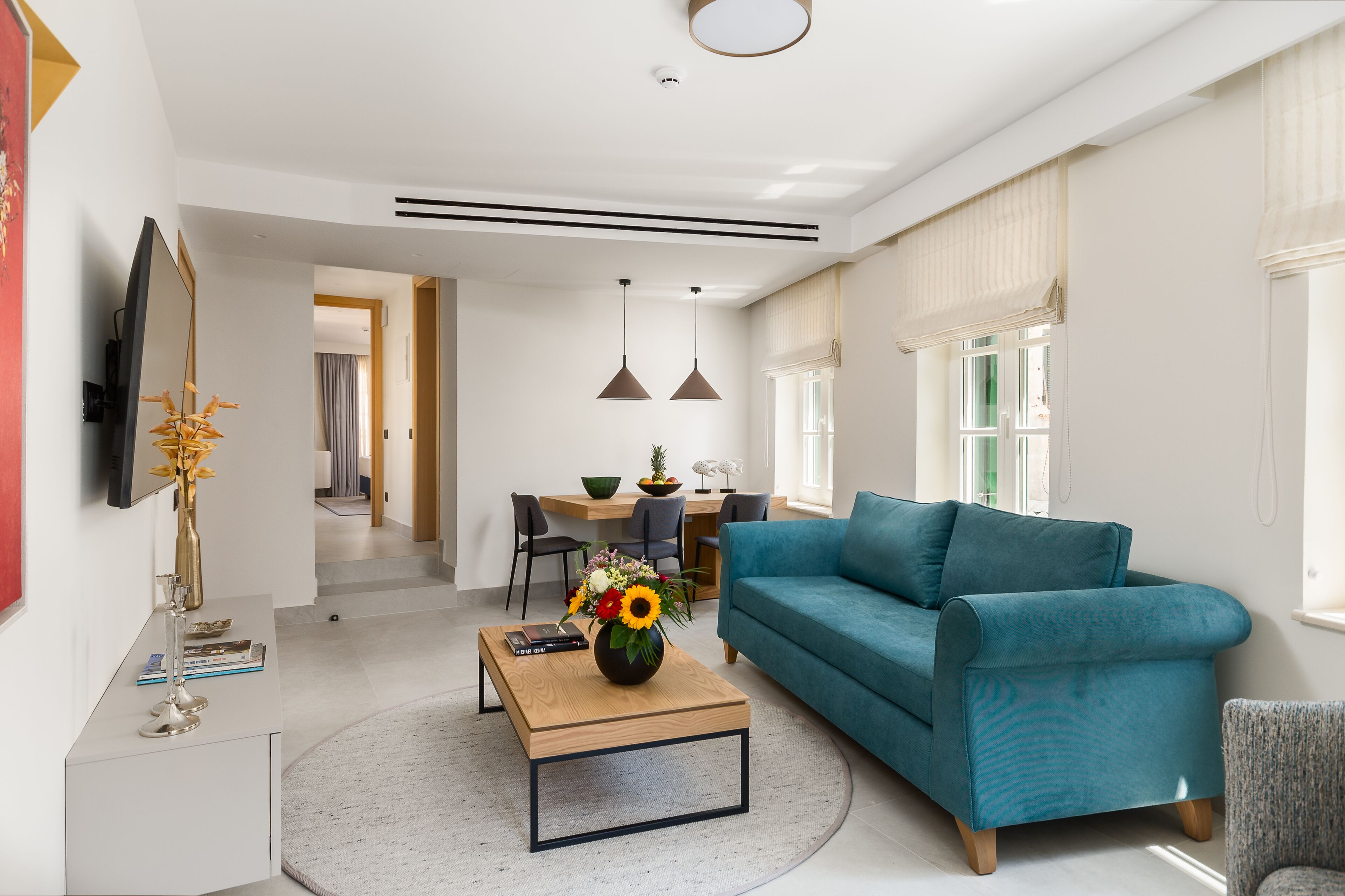 A modern living room with a teal sofa, a coffee table with a vase, and a flat-screen TV mounted on the wall.