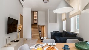 Een moderne woonkamer met een eethoek, met een bank, een televisie en een ontbijtje met croissants en sap.